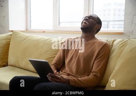 Cheerful black man laughing watching videos online on digital tablet Stock Photo