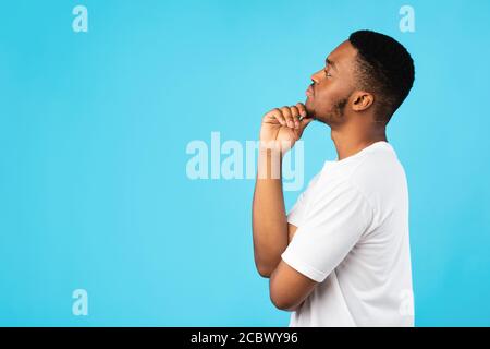 Thoughtful Black Guy Thinking Looking Aside Standing On Blue Background Stock Photo
