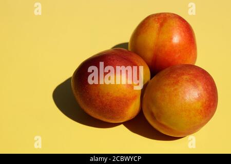 Three ripe nectarines on yellow background. Stock Photo