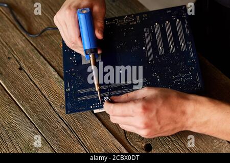 Technician or engineer is focused on repairing electronic circuit board with soldering iron. Man hands soldiers computer circuit board using soldering Stock Photo