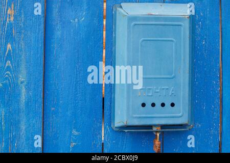 An old blue Soviet mailbox with the inscription Mail and a rusty lock hanging on a rural wooden blue fence. Stock Photo