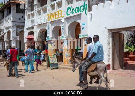 Men riding donkeys on the main street of Lamu town in Lamu Island, Kenya. Stock Photo