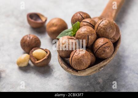 Pile macadamia nuts open kernels and shells in spoon  on stone background. Stock Photo