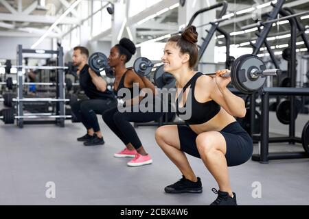 sportive people, multiethnic group perform exercises with heavy weights in gym. young diverse man and women workout, have muscular body