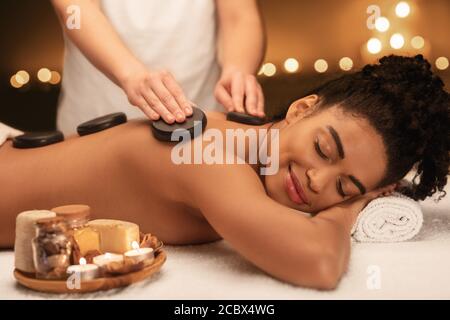 Spa therapist putting black stones on lady back Stock Photo