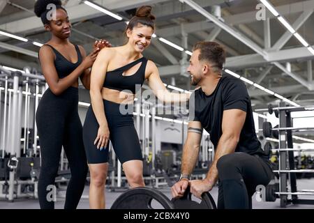 two athletic diverse women talking with trainer in the gym, they communicate, discuss something, smile. healthy lifestyle concept Stock Photo