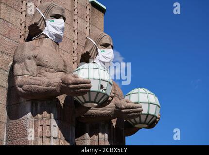 Helsinki, Finland - 16 August 2020: Iconic stone men statues by the side of the entrance to the Helsinki Central Railway Station decorated as wearing Stock Photo