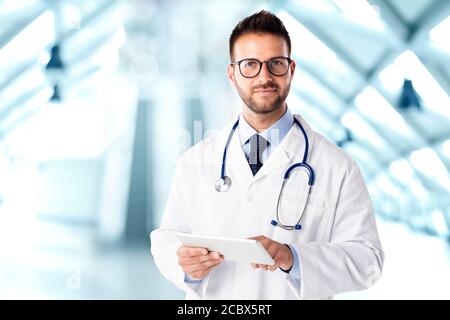 Shot of male doctor standing on the clinic’s foyer and using digital tablet while working. Stock Photo
