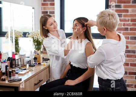 professional make-up artist and hair stylist work together in beauty salon, beautiful model came to get fashionable make-up and hairstyle for wedding. Stock Photo