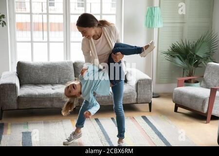 Happy young mother holding little laughing kid daughter upside down. Stock Photo