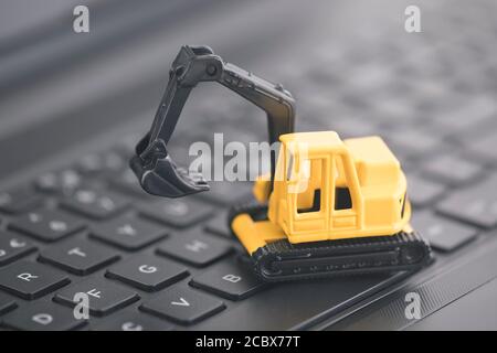 Excavator miniature working on black laptop keybaord Stock Photo