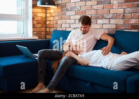 careful handsome man stroke belly of pregnant wife, married couple spend weekends at home, have rest. man and woman in domestic wear, pajamas Stock Photo