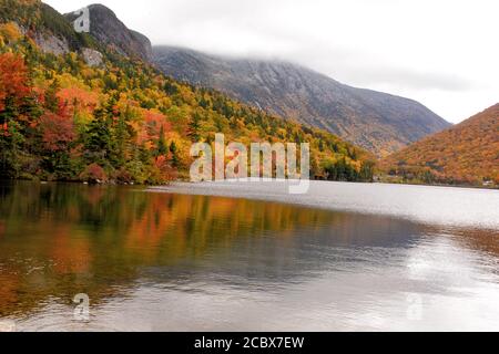 Autumn in White Mountains of New Hampshire. Sweeping view of Franconia Notch and colorful foliage from shore of Echo Lake. Dusting of snow on mountain Stock Photo