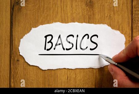 Male hand writing 'basics' on white paper on wooden table. Business concept. Stock Photo