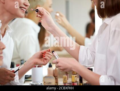 side view on make-up artist going to apply lipstick on smiling girl, doing make-up in beauty studio Stock Photo