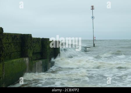 Waves from the incoming tide seen breaking on the groynes on Hunstanton beach. Stock Photo