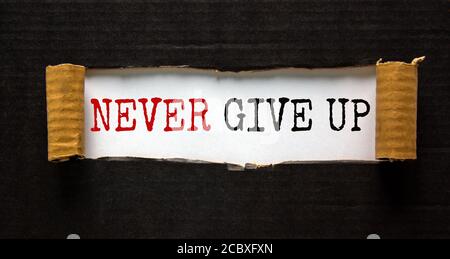 The words 'never give up' appearing behind torn black paper. Beautiful background. Business concept. Stock Photo