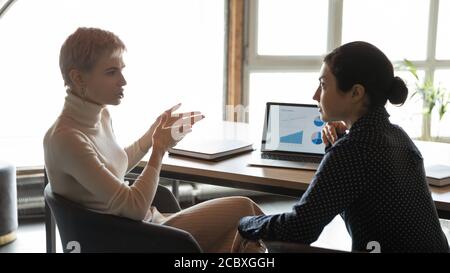 Serious young blonde company leader discussing statistics with indian employee. Stock Photo