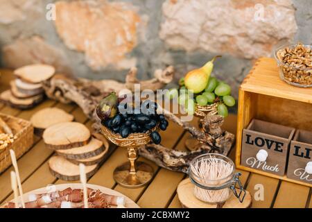 Large blue and white grapes in bowls with pear and figs on a wooden table with ham and walnut kernels. Stock Photo