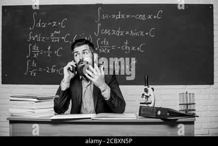 Calling parents. Call colleague ask advice. Teacher bearded man talk mobile phone. Pedagogue keep in touch with colleagues. School teacher call mobile phone while sit classroom chalkboard background. Stock Photo