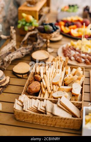Wicker bread and cereal tray with sliced loaf, bread sticks and cookies on a wooden holiday table. Stock Photo