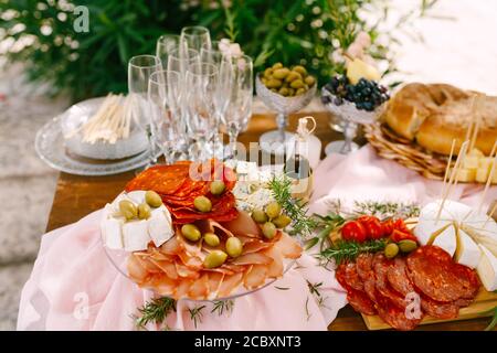 Plate with chorizo sausage, ham and brie and Dorblu cheeses in olives on a table served for a banquet on a blurred background. Stock Photo