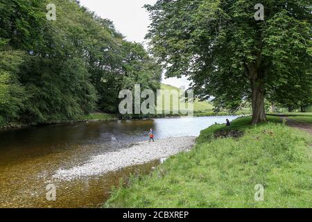 Boy skimming stones River Wharfe, Hebden, North Yorkshire whilst mother watches Stock Photo