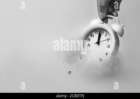 A hand holds alarm clock with dispersion effect on white background. Passing away concept. Top view. Flat lay. Selective focus. A concept of the time Stock Photo