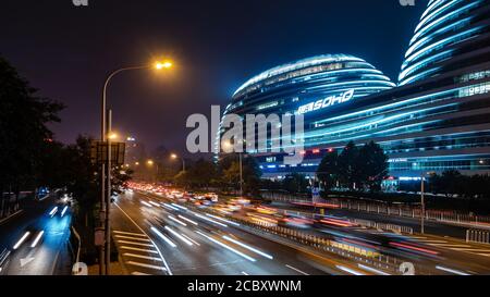 Night traffic on highway next to modern architectural landmark Galaxy SOHO urban complex in Beijing, China. Stock Photo