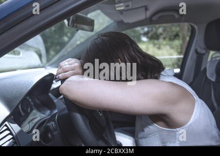 Young female driver at the wheel of her car, super tired, falling asleep while driving in a potentially dangerous situation - Road safety concept Stock Photo