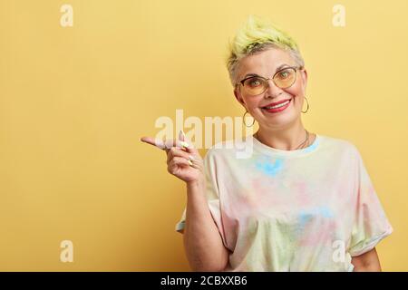 stylish woman showing something with index finger, look here, isolated yellow background, studio shot. copy space, beauty salon. direction concept Stock Photo