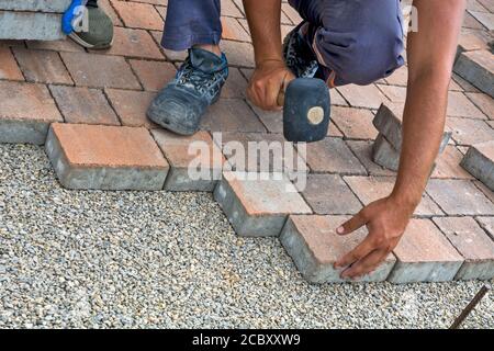 Master lay and install floor bricks on a public surface. The base is small stone and they fit concrete decorative pieces of brick. Stock Photo