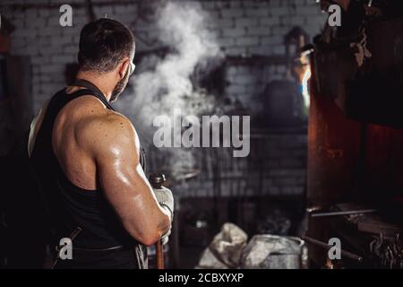 side view on unrecognizable forger bodybuilder, strong man, heating and preparing metal for manufacturing Stock Photo
