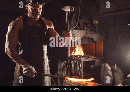 muscular adult with beard wearing leather apron working in workshop, heating. hardened metal in furnace Stock Photo
