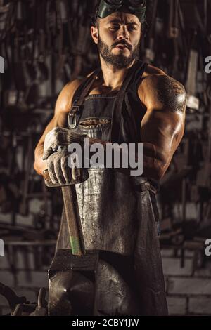 cool caucasian and young blacksmith portrait. forger in work with metal, powerful bodybuilder, strong muscular body Stock Photo