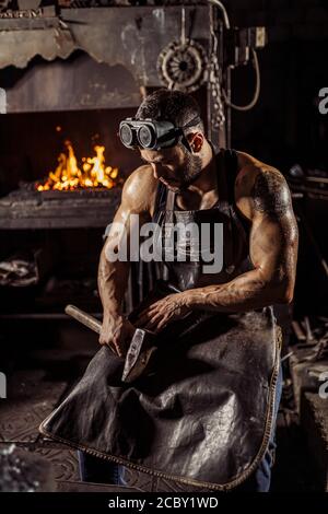 portrait of strong muscular handsome forger in leather uniform isolated in workshop, furnace fire in the background Stock Photo