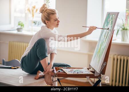 talented painter sitting with crossed legs and enjoying her pastime. full length side view photo Stock Photo