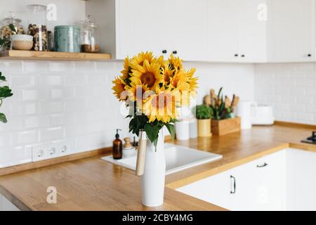 sunflowers bouquet in vase on the kitchen, selective focus. Clean white simple modern kitchen in scandinavian style on background Stock Photo