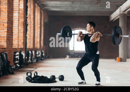 Handsome man doing squats with barbell in the sport center. guy is fond of professional sport. full length photo. copy space Stock Photo