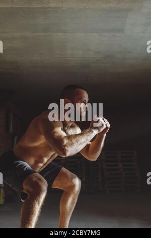 Strong angry athletic man doing the exercises with kettlebells on dark ...
