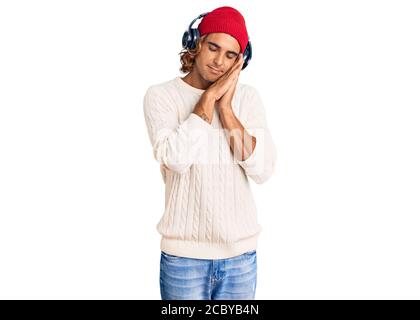 Young hispanic man listening to music using headphones sleeping tired dreaming and posing with hands together while smiling with closed eyes. Stock Photo