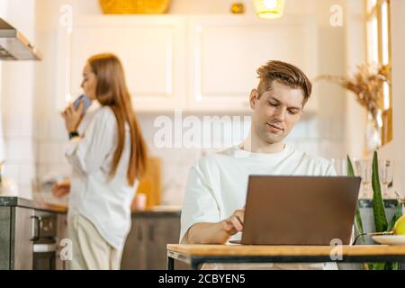 young caucasian woman talk on phone while her husband work in laptop, freelance work. married couple busy with their own business, quarantine during c Stock Photo