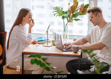 beautiful caucasian wife doing make-up while her husband work at home, they sit together, talk and support. at morning. family, job, work, freelance c Stock Photo