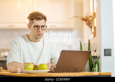 young caucasian guy work from home, he use laptop. man in domestic wear, surf the Net, developing new business project at home. freelance, job,work co Stock Photo