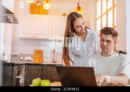 beatiful wife support her husband suring his work from home, he is in freelance.young businessman works even in weekends, using laptop Stock Photo