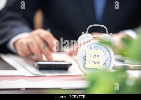 Alarm clock with tax time note and Businessmen using calculators. Stock Photo