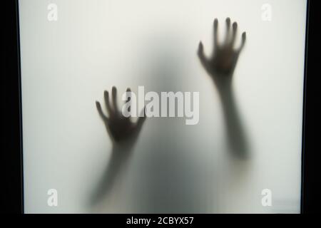 The dark shadow of the hands and body behind the opaque glass makes it look scary in the Halloween concept. Stock Photo