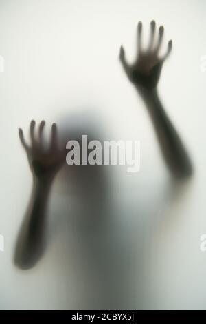The dark shadow of the hands and body behind the opaque glass makes it look scary in the Halloween concept. Stock Photo