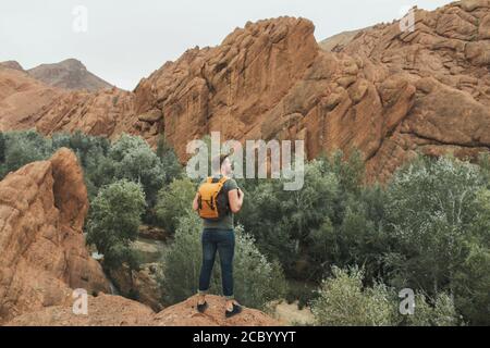 Backpacker man explore Todra gorge canyon in Morocco. Red color mountains formed by weathering. Travel in Africa concept. Stock Photo