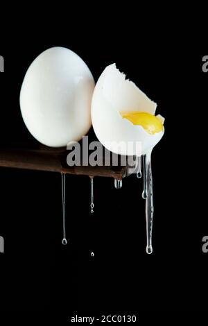 Chicken eggs, one egg is broken in which the yolk is visible and the white flows down on a black background. Stock Photo